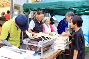 盆踊りで串もちを焼いて提供している様子の写真です。